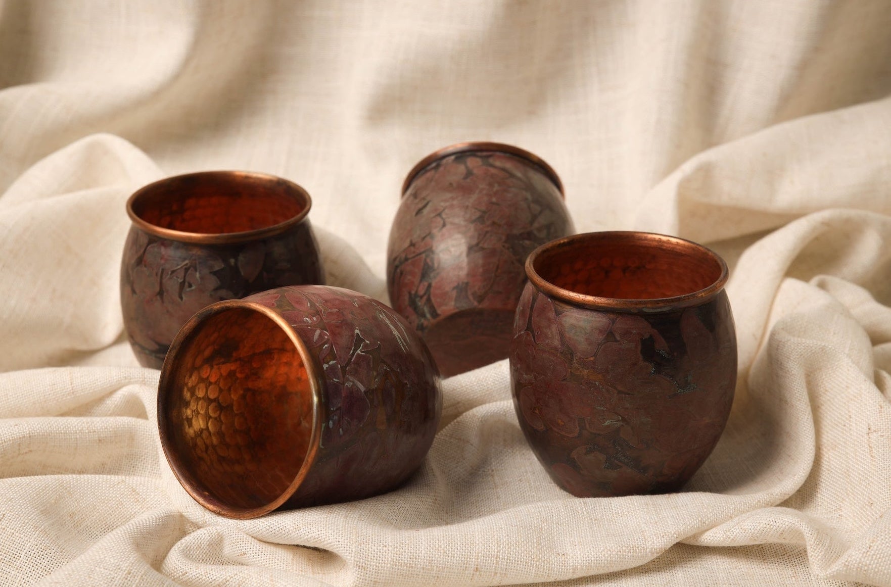 Four copper cups on a textured beige fabric background