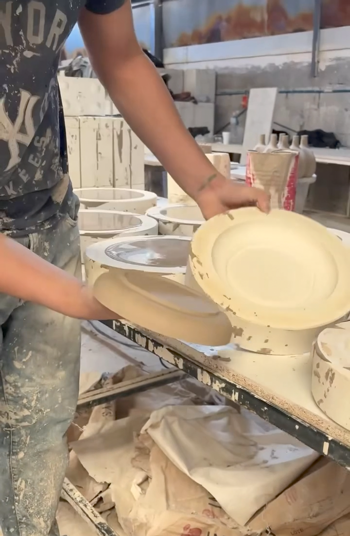 Person holding a ceramic plate in a pottery studio with various ceramic items and tools.