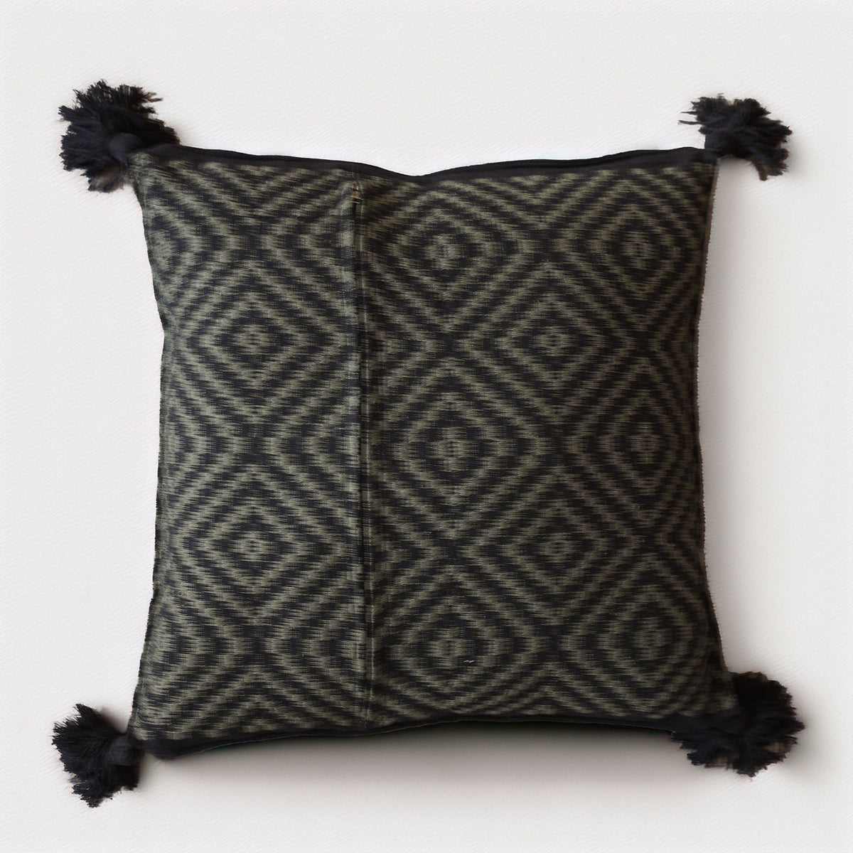 A square throw pillow with a black and dark gray geometric diamond pattern, finished with black tassels on all four corners, shown against a plain off-white background.
