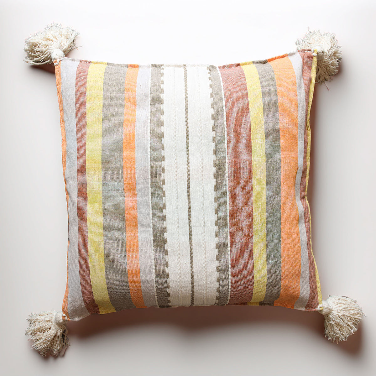 A square decorative throw pillow with vertical stripes in orange, yellow, white, gray, and dusty pink, finished with four cream tassels at the corners, shown against a plain off-white background.